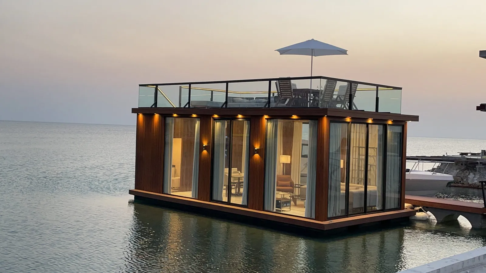Floating Majlis lit warmly at dusk beside a moored yacht