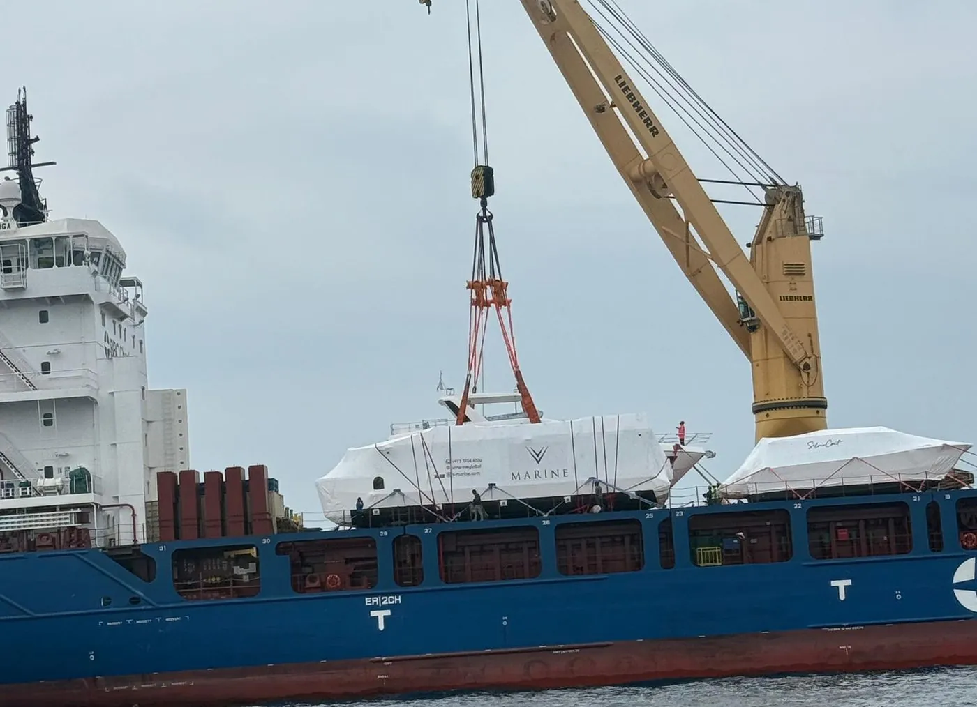 A wrapped V-Marine hull lifted onto a cargo ship's deck by the ship's crane