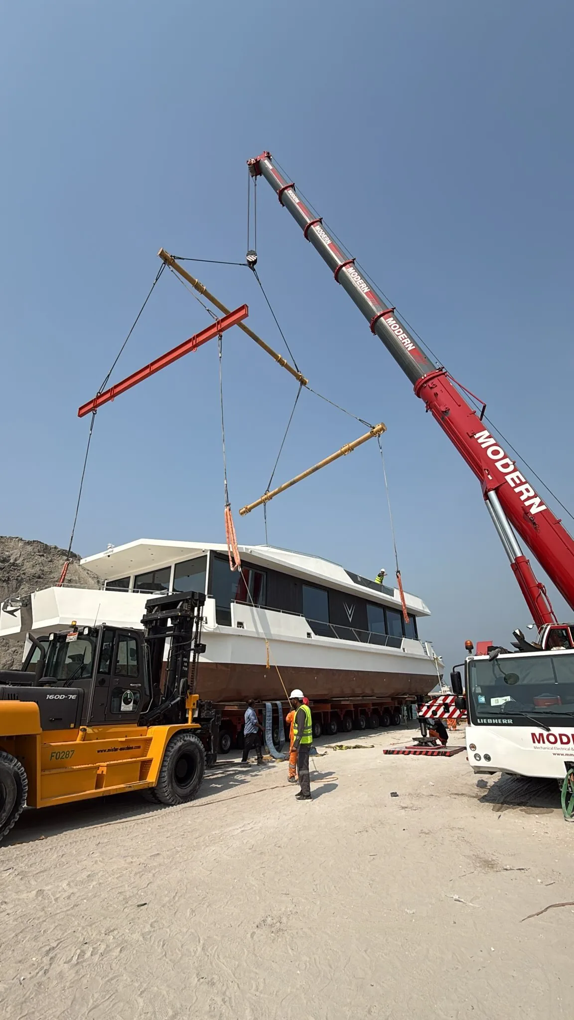 A finished V-Marine hull on multi-axle trailers with a mobile crane alongside